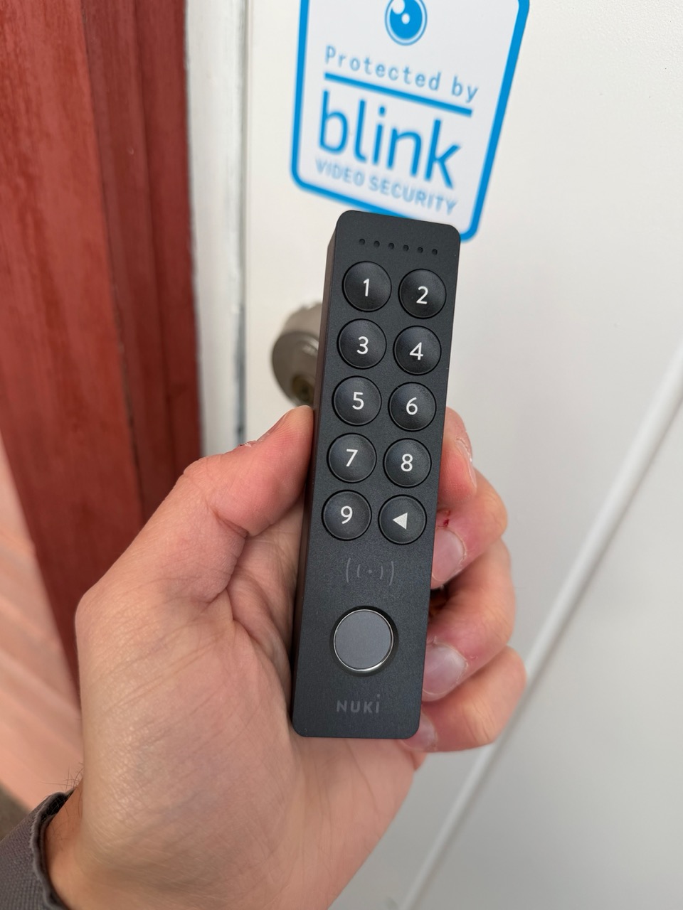 Nuki Keypad 2 NFC in hand, with Blink sticker on door behind