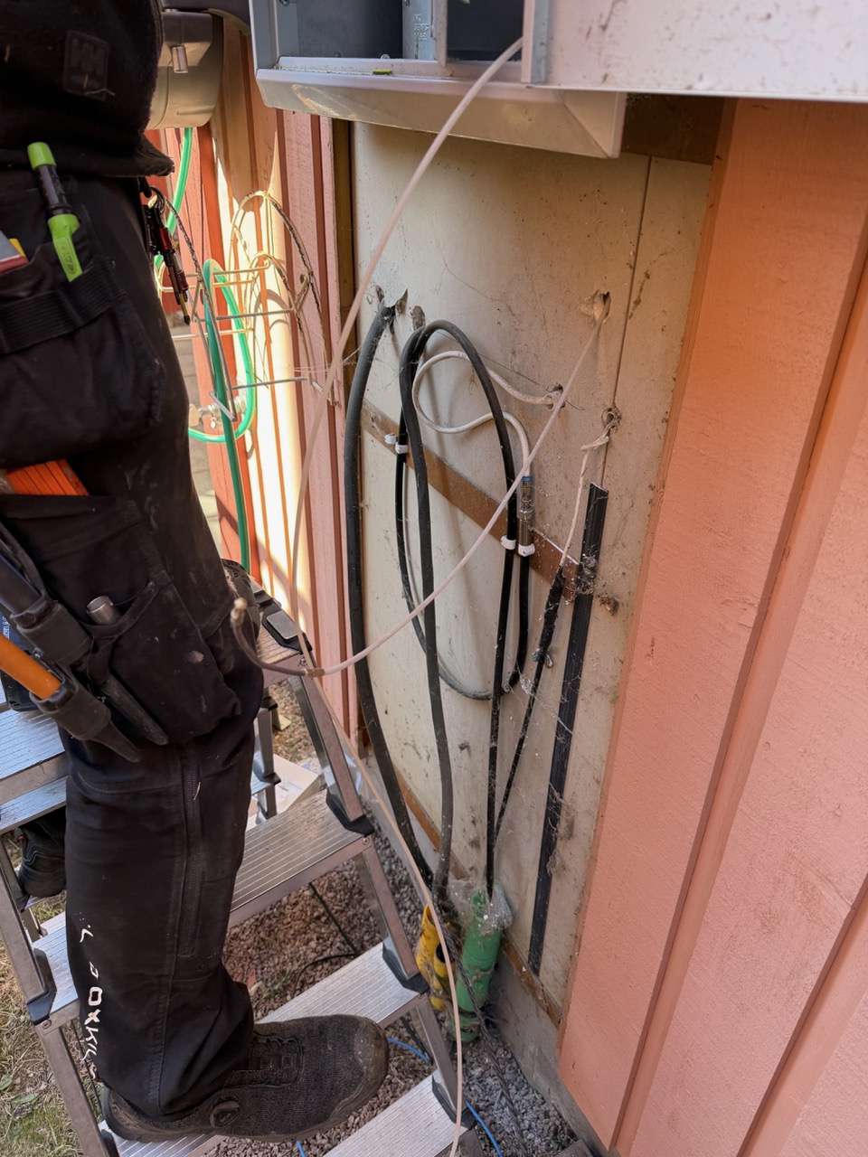 Magnus on a ladder at the top of the fuse box, pulling cable through the exterior conduit