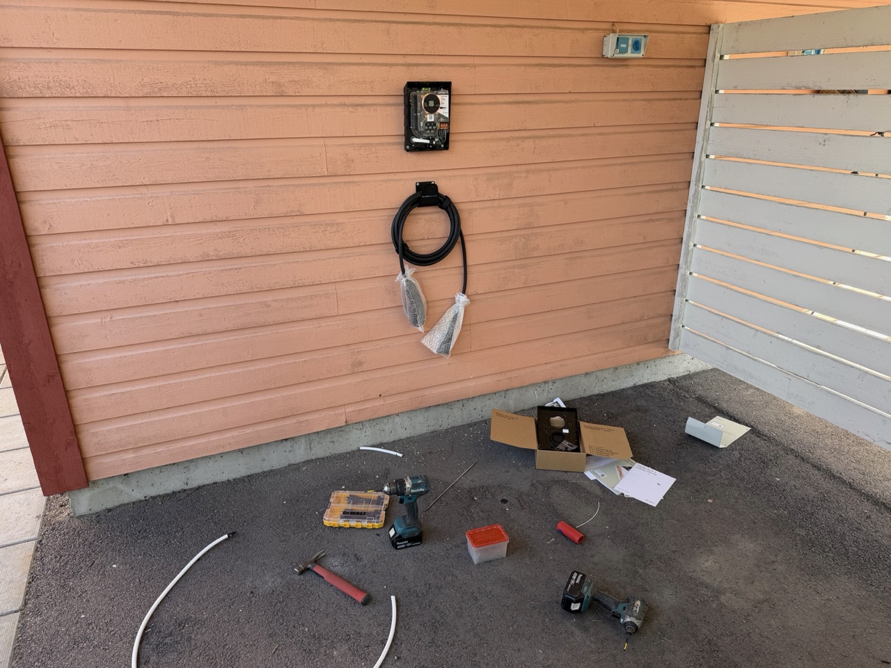 Zaptec Go 2 partially mounted on the carport wall with mounting plate exposed and tools laid out