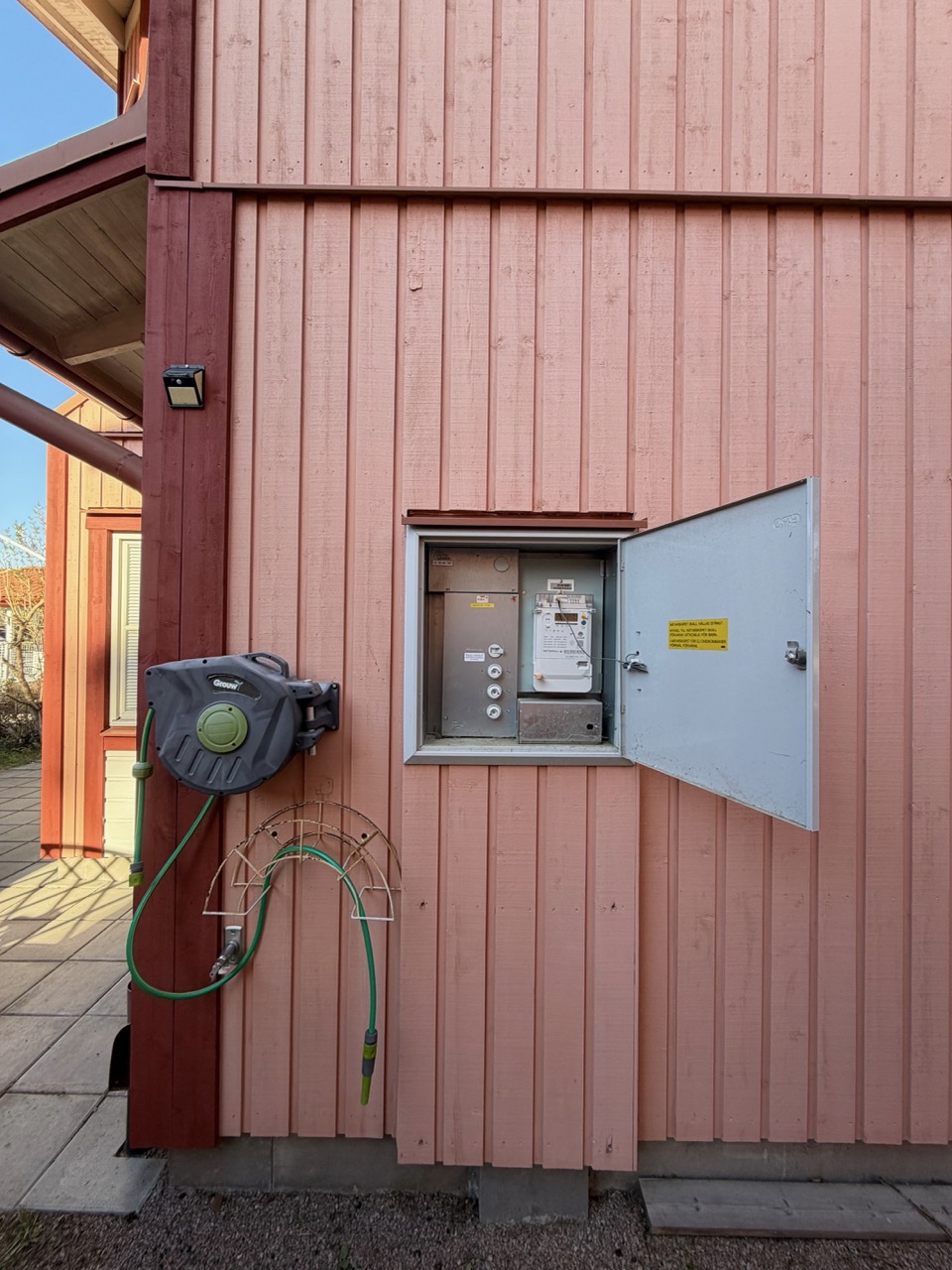 Wide exterior shot of the closed fuse box on the side of the red wooden house